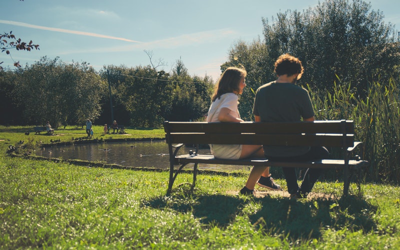 2 people sitting on bench near pond