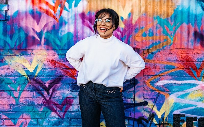 joyful woman standing in front of multicoloured wall